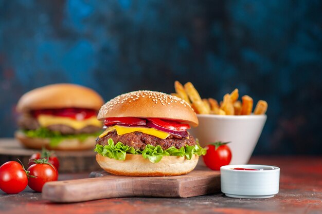 Vista frontale deliziosi cheeseburger di carne con pomodori e patatine fritte al buio