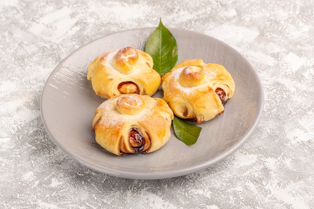 Vista frontale deliziosi dolci fruttati dolci al forno con foglie verdi sulla superficie grigia torta pasticceria dolce cuocere il tè