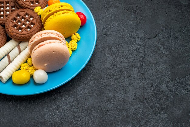 Vista frontale deliziosi macarons francesi con caramelle e biscotti al cioccolato su scrivania grigia biscotto zucchero torta dolce cuocere i biscotti