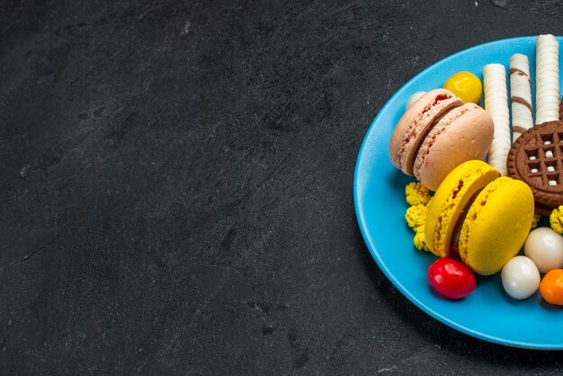 Vista frontale deliziosi macarons francesi con caramelle e biscotti al cioccolato su scrivania grigia biscotto zucchero torta dolce cuocere il biscotto