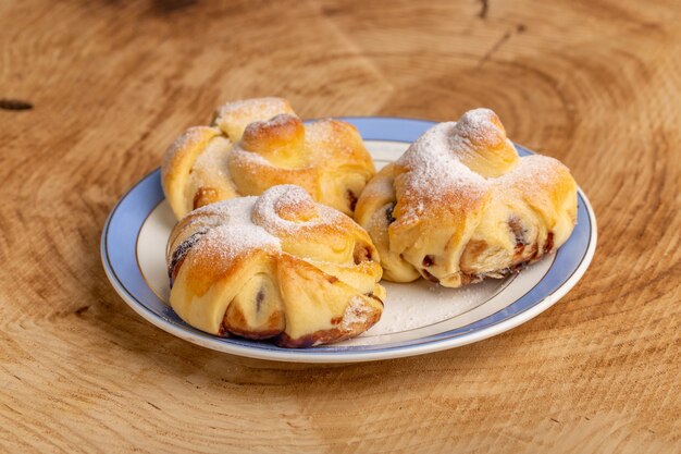 Vista frontale deliziosi pasticcini con ripieno all'interno del piatto sul tavolo di legno, dolce zucchero torta cuocere pasticceria frutta