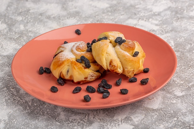 Vista frontale deliziosi pasticcini con ripieno all'interno della piastra insieme a frutta secca sul tavolo bianco, torta di zucchero dolce cuocere pasticceria