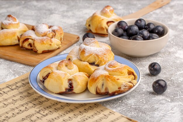 Vista frontale deliziosi pasticcini con ripieno all'interno della piastra insieme a prugnoli freschi sul tavolo bianco, pasticceria da forno torta dolce