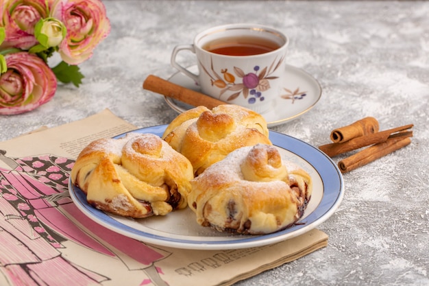 Vista frontale deliziosi pasticcini con ripieno all'interno della piastra insieme a tè e cannella sul tavolo bianco, torta di zucchero dolce cuocere la frutta della pasticceria