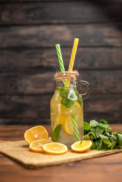 Vista frontale dell'acqua detox fatta di limone e menta su un vecchio giornale su fondo di legno marrone