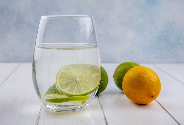 Vista frontale dell'acqua in un bicchiere con lime e limone su una superficie bianca