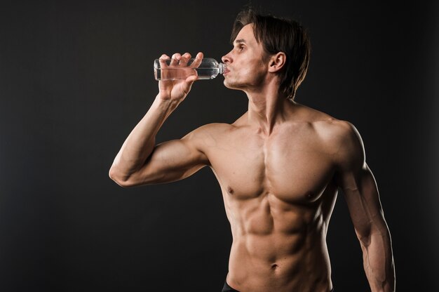 Vista frontale dell'acqua potabile dell'uomo senza camicia atletico