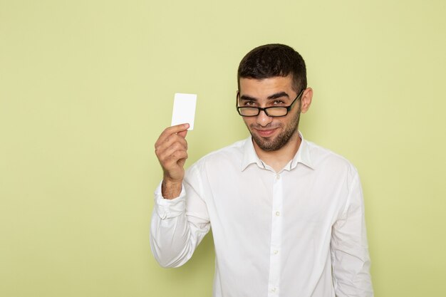 Vista frontale dell'impiegato di ufficio maschio in carta bianca della tenuta della camicia con il sorriso sulla parete verde chiaro