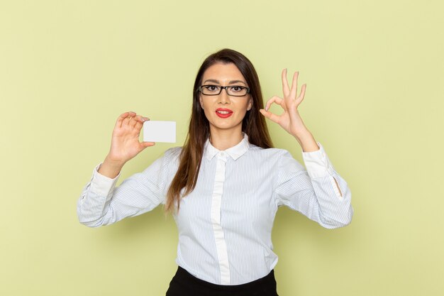 Vista frontale dell'impiegato femminile in camicia bianca e gonna nera che tiene carta di plastica bianca sulla parete verde chiaro