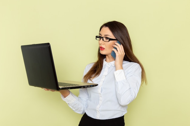 Vista frontale dell'impiegato femminile in camicia bianca e gonna nera che tiene e che utilizza computer portatile sulla donna di lavoro di lavoro di lavoro di affari dell'ufficio della scrivania verde