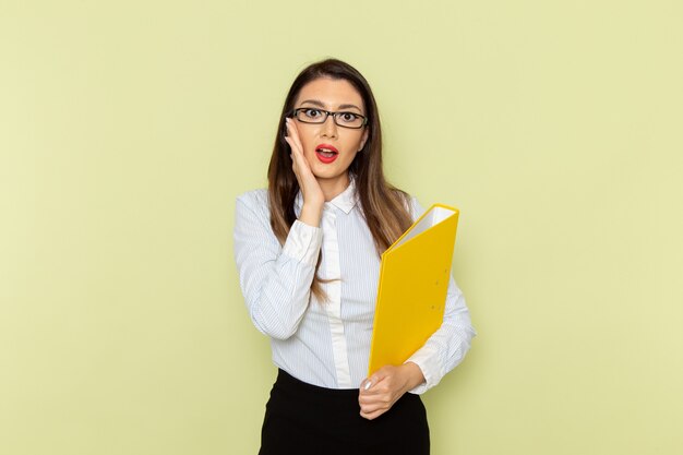 Vista frontale dell'impiegato femminile in camicia bianca e gonna nera che tiene file di colore giallo sulla parete verde