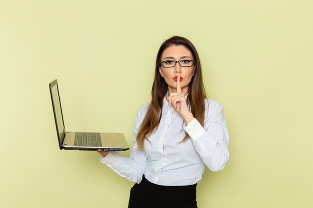 Vista frontale dell'impiegato femminile in camicia bianca e gonna nera che tiene laptop sulla parete verde chiaro