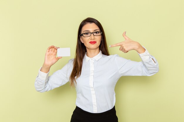 Vista frontale dell'impiegato femminile in camicia bianca e gonna nera che tiene scheda bianca sulla parete verde chiaro