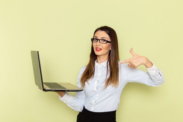 Vista frontale dell'impiegato femminile in camicia bianca e gonna nera che tiene utilizzando il computer portatile sulla parete verde