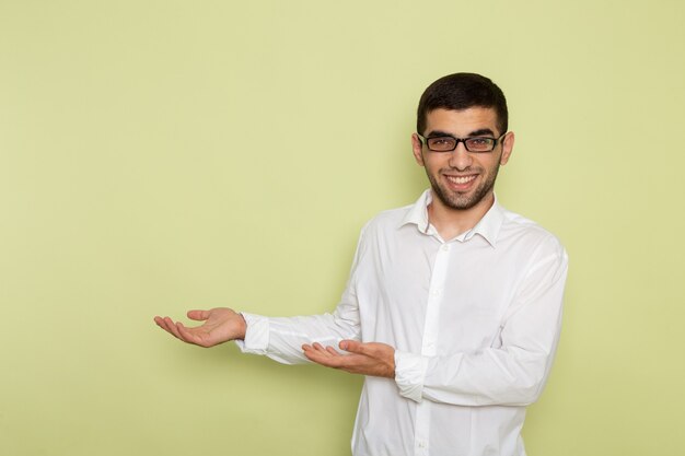 Vista frontale dell'impiegato maschio in camicia bianca che sorride e che posa sulla parete verde