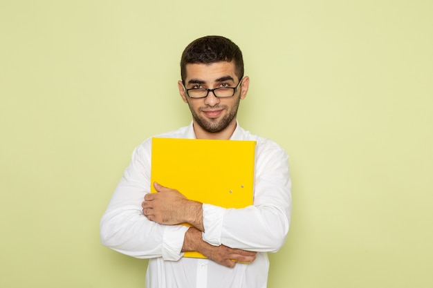 Vista frontale dell'impiegato maschio in camicia bianca che tiene archivi gialli che sorridono sulla parete verde