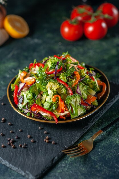 Vista frontale dell'insalata vegana con ingredienti freschi in un piatto e pepe su tagliere nero