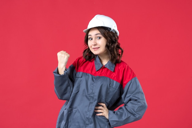 Vista frontale dell'orgoglioso costruttore femminile in uniforme con elmetto su sfondo rosso isolato