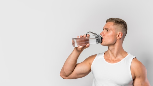 Vista frontale dell'uomo adatto che beve dalla bottiglia di acqua