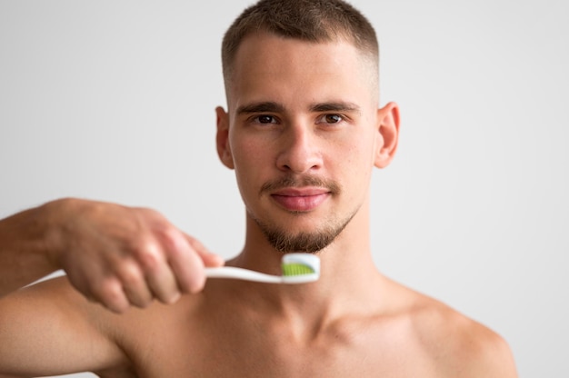 Vista frontale dell'uomo bello che tiene lo spazzolino da denti con dentifricio in pasta