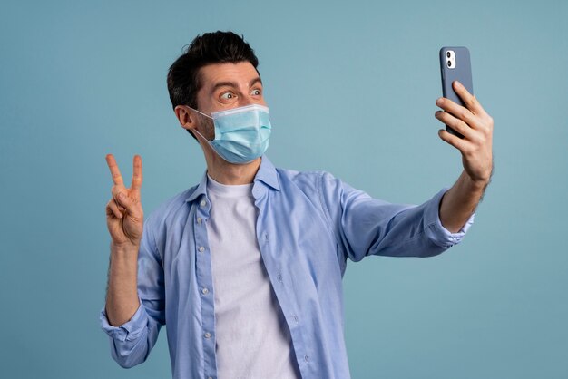 Vista frontale dell'uomo che indossa la mascherina medica e prendendo selfie mentre fa il segno di pace