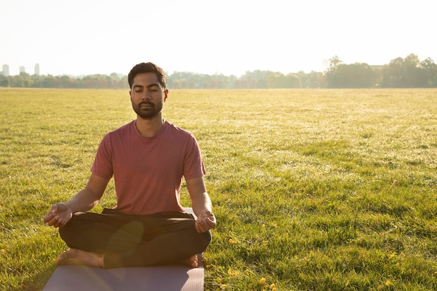 Vista frontale dell'uomo che medita all'aperto sul tappetino da yoga