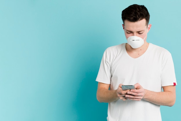 Vista frontale dell'uomo con la mascherina medica che osserva in su coronavirus sullo smartphone