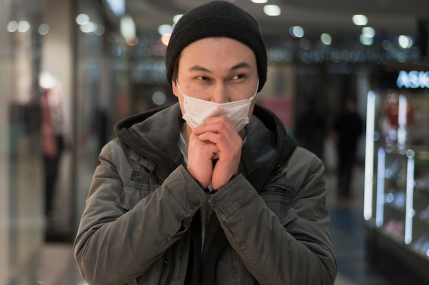 Vista frontale dell'uomo con la mascherina medica che prega al centro commerciale