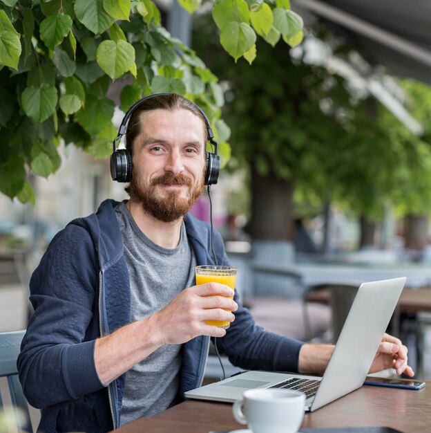 Vista frontale dell'uomo con succo in una terrazza con cuffie e laptop