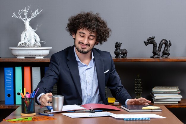 Vista frontale dell'uomo d'affari sorridente che beve tè seduto alla scrivania in ufficio