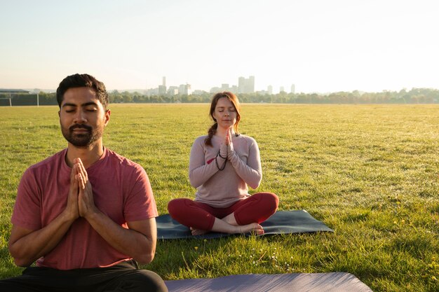 Vista frontale dell'uomo e della donna che meditano all'aperto su stuoie di yoga