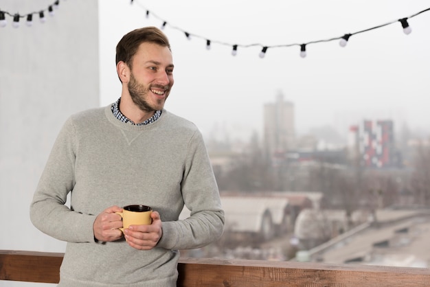 Vista frontale dell'uomo in maglione che tiene tazza in mani a casa