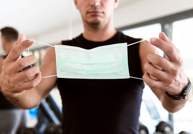 Vista frontale dell'uomo in palestra che tiene mascherina medica durante la pandemia