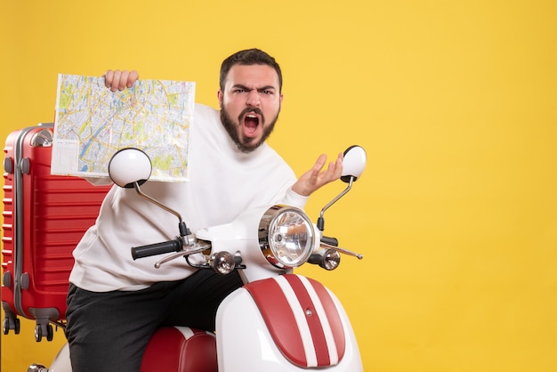 Vista frontale dell'uomo nervoso seduto sulla moto con la valigia sopra che tiene la mappa su sfondo giallo isolato