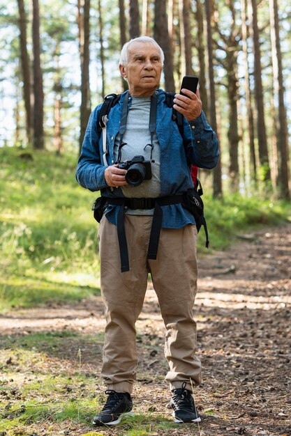 Vista frontale dell'uomo più anziano ad esplorare la natura con smartphone e fotocamera