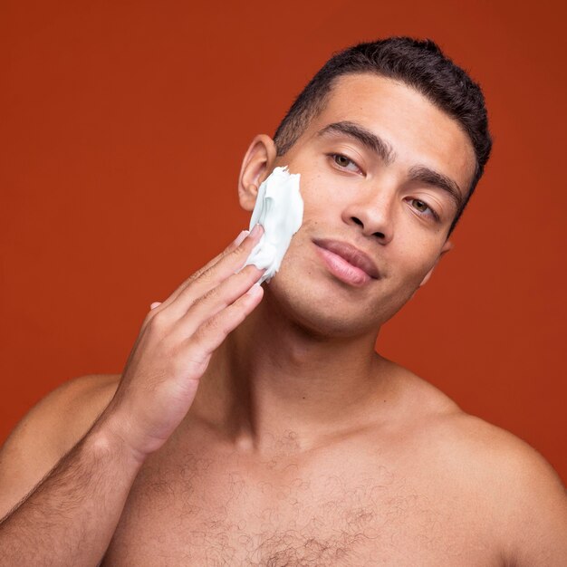 Vista frontale dell'uomo senza camicia bello che applica schiuma da barba