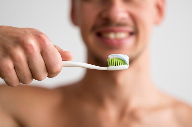 Vista frontale dell'uomo sfocato che tiene uno spazzolino da denti con dentifricio in pasta