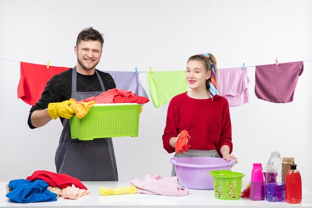 Vista frontale dell'uomo sorridente e sua moglie che tengono un cesto della biancheria e una tinozza di plastica in piedi dietro il tavolo cesti della biancheria e il lavaggio degli animali sul tavolo