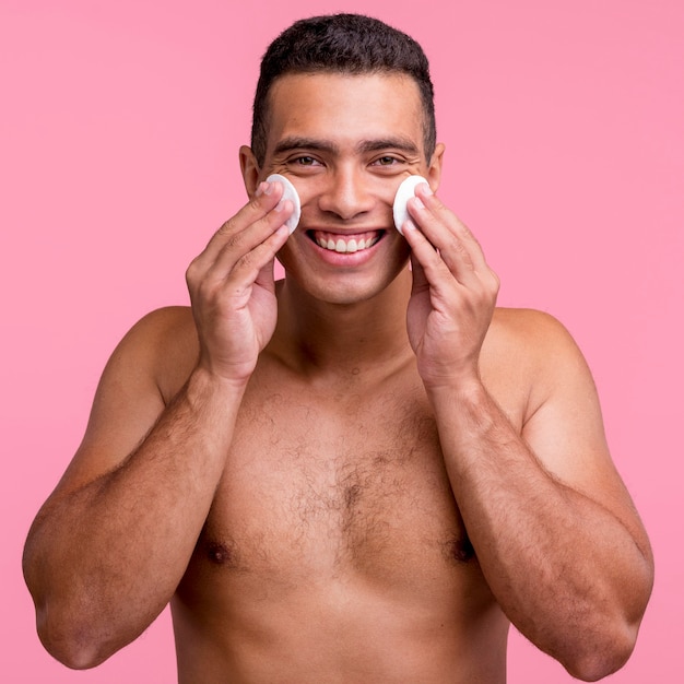 Vista frontale dell'uomo sorridente utilizzando tamponi di cotone sul viso