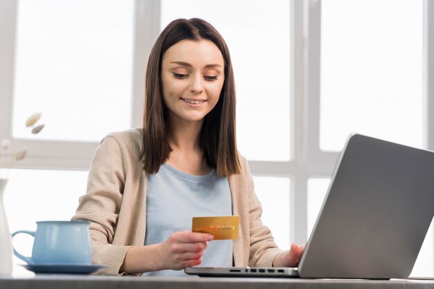 Vista frontale della carta di credito della tenuta della donna e lavorare al computer portatile