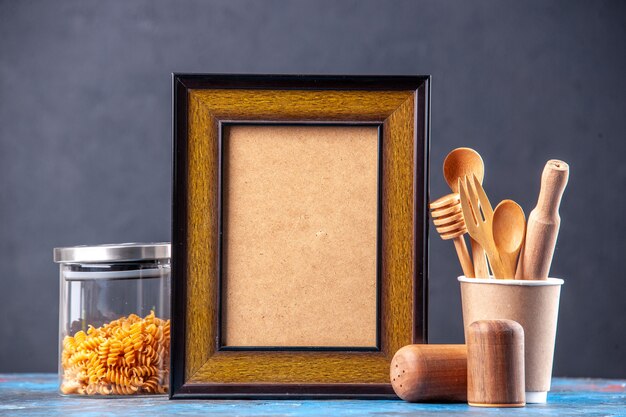 Vista frontale della cornice vuota all'interno di diverse spezie pasta in una pentola di vetro cucchiai di legno sul tavolo blu