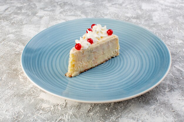 Vista frontale della deliziosa fetta di torta all'interno del piatto rotondo blu con crema e frutti rossi sulla superficie grigia