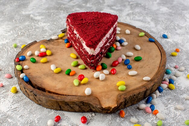 Vista frontale della deliziosa fetta di torta con crema e frutta sulla scrivania in legno con caramelle colorate
