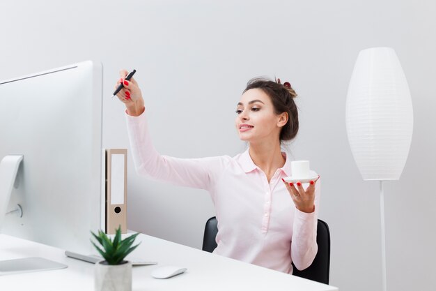 Vista frontale della donna allo scrittorio che tiene tazza di caffè