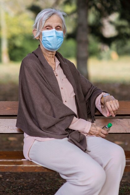 Vista frontale della donna anziana con maschera medica e disinfettante per le mani