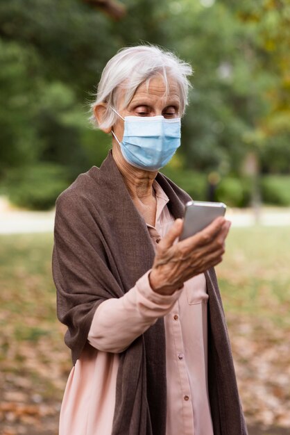 Vista frontale della donna anziana con maschera medica e smartphone
