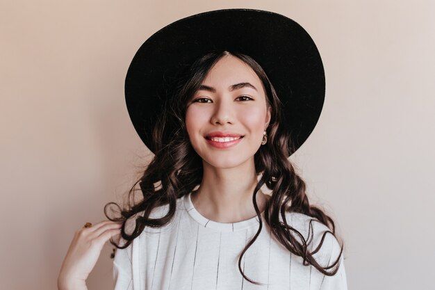 Vista frontale della donna asiatica sorridente allegra. Studio shot di felice donna coreana che indossa il cappello nero.