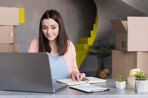 Vista frontale della donna che lavora al computer portatile con le scatole nella parte posteriore