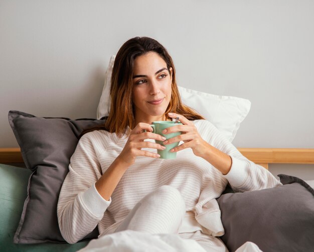 Vista frontale della donna che mangia il caffè a letto