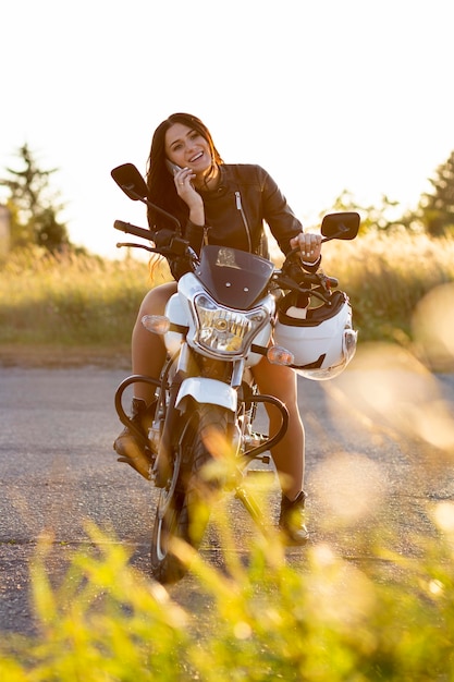 Vista frontale della donna che parla sullo smartphone mentre riposa sulla sua moto